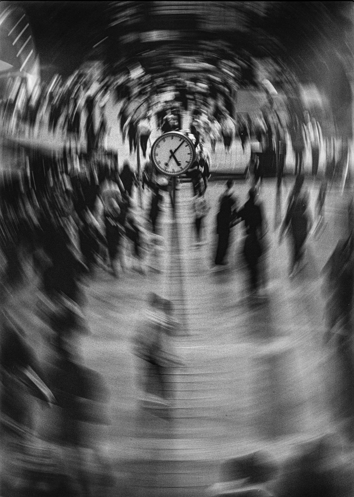 A clock at the center of a busy train station captured with a radial zoom blur, symbolizing the relentless passage of time